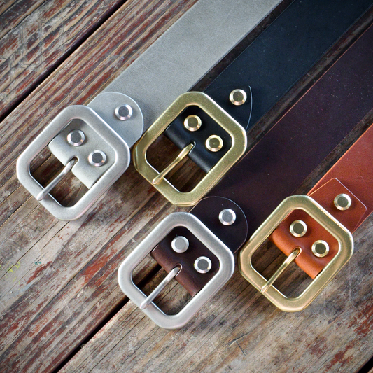 Four leather belts with different buckles on a wooden surface