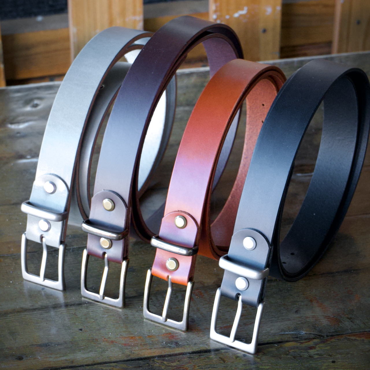 Four leather belts in different colors on a wooden surface