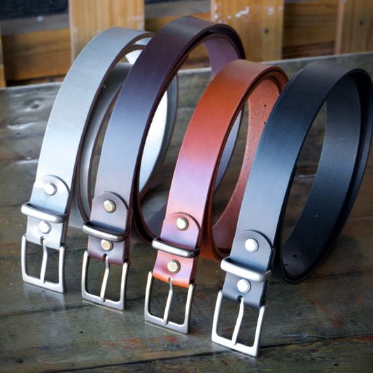 Four leather belts in different colors on a wooden surface