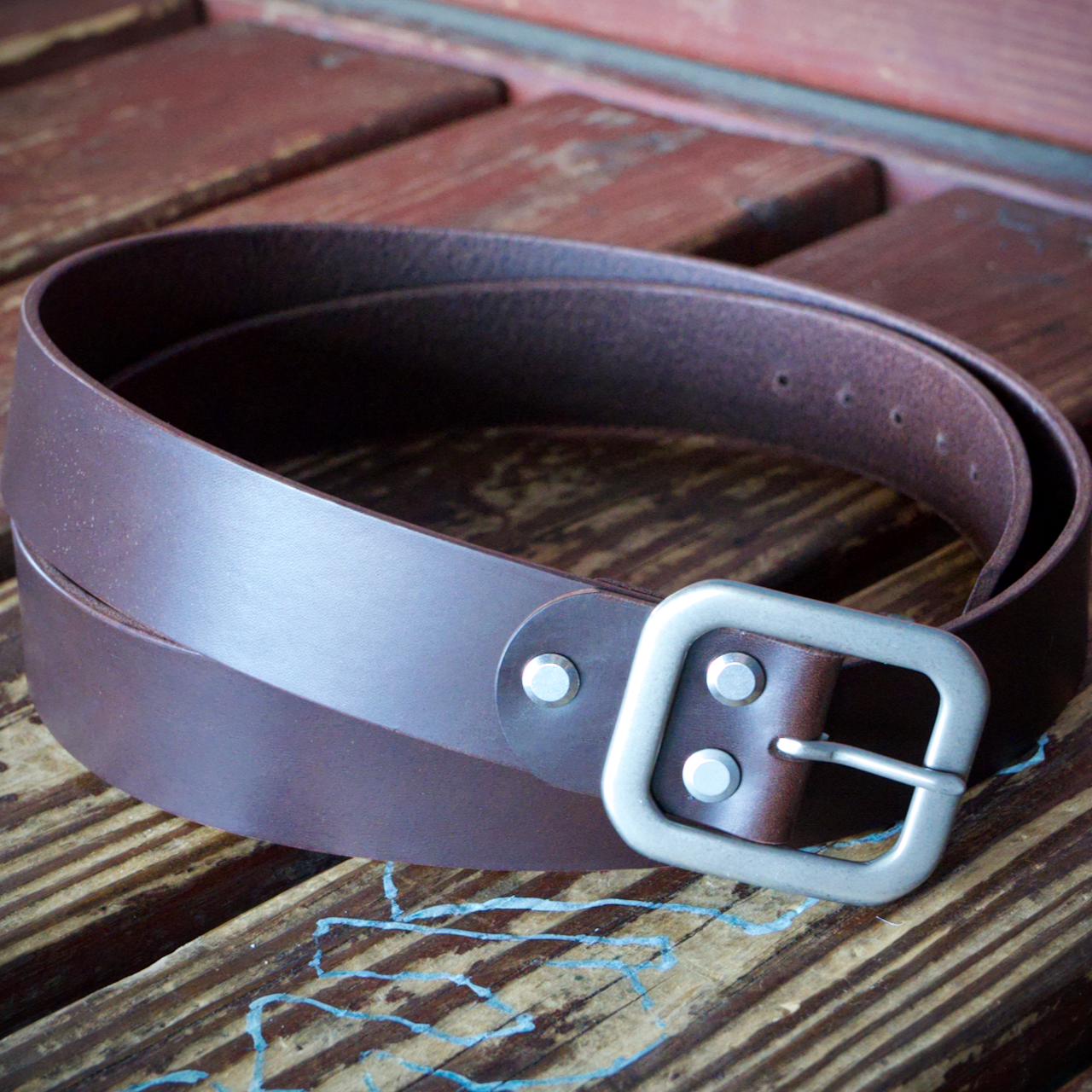 Brown leather belt with a silver buckle on a wooden surface