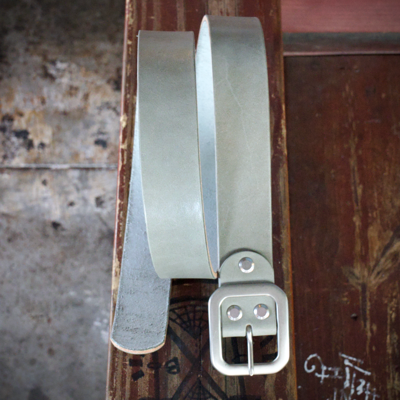 Light gray leather belt with a silver buckle on a textured surface