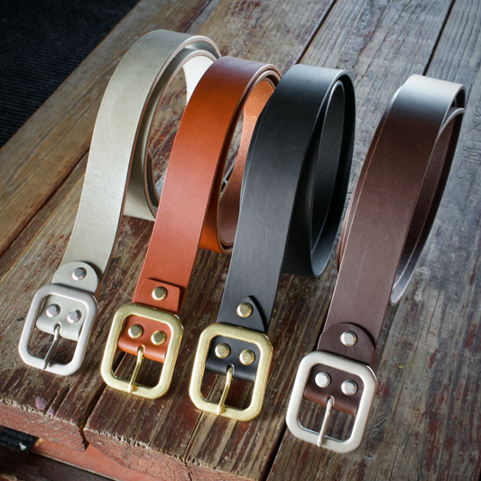 Five leather belts with different colors and buckles on a wooden surface